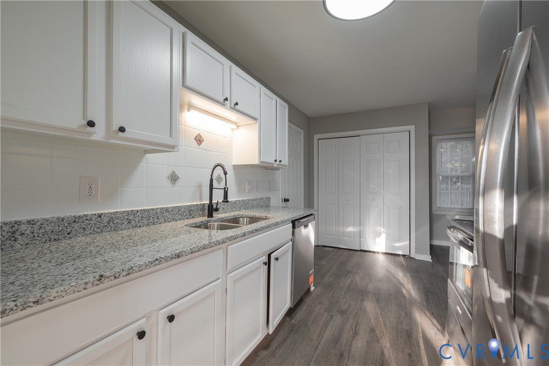 Kitchen featuring white cabinetry, granite countertops, stainless steel appliances, a high-arc faucet, and wood-finish flooring