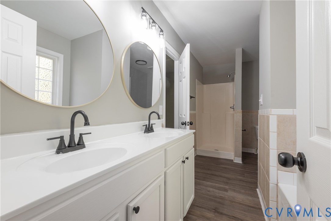 Dual-sink vanity with white cabinetry, light-toned countertop, matte black fixtures, circular wall-mounted mirrors, and wood-finish flooring