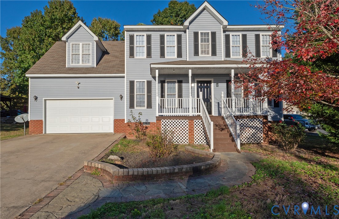 Two-story residence featuring vinyl siding, a brick foundation, a front covered porch with railings, and a concrete driveway