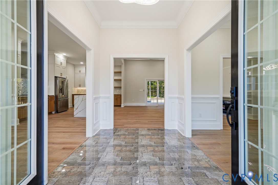 Entryway featuring polished stone tile flooring, wood-finish flooring, wainscoting, and crown molding