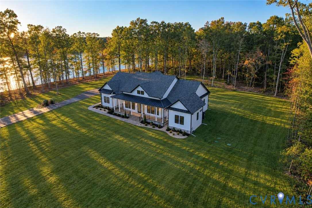 Contemporary residence featuring a multi-gabled roofline, covered front porch, asphalt shingle roofing, paved driveway, and expansive lawn situated on a waterfront lot