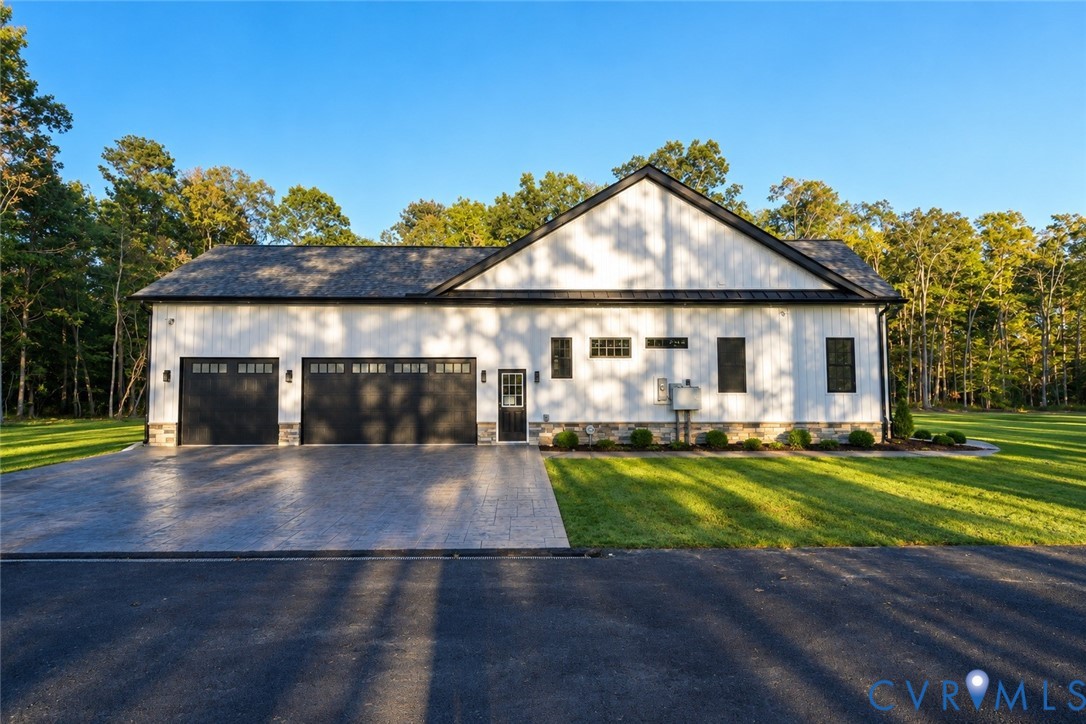 Board and batten exterior with stone veneer foundation, multi-car garage with glass-paneled doors, stamped concrete driveway, and asphalt shingle roof