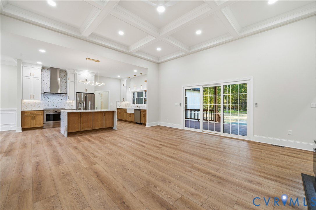 Coffered ceiling, wood-finish flooring, kitchen island with stone countertop, stainless steel appliances, and sliding glass doors to the exterior deck