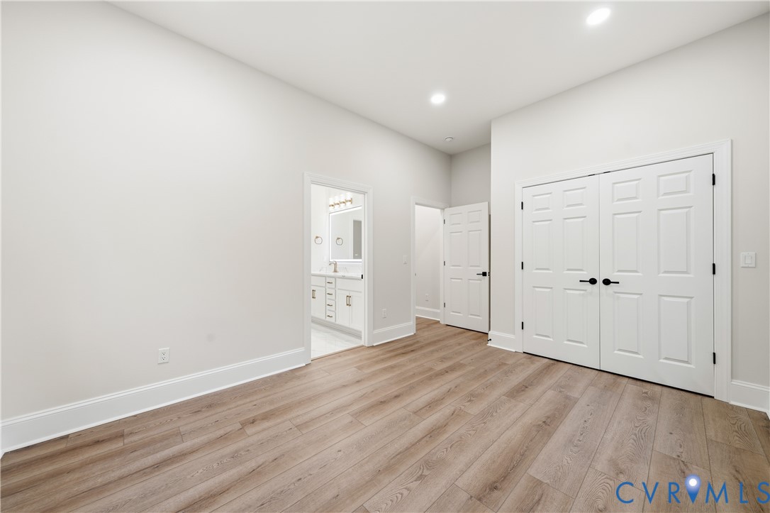 Room featuring neutral wall paint, wood-finish flooring, recessed lighting, white six-panel interior doors with matte black hardware, and double-door reach-in closet