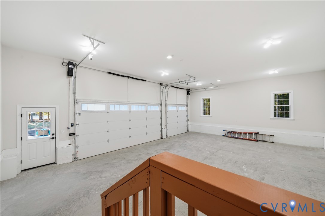Spacious three-car garage featuring a concrete floor, high-clearance overhead doors with glass panels, interior pedestrian door, and multiple windows