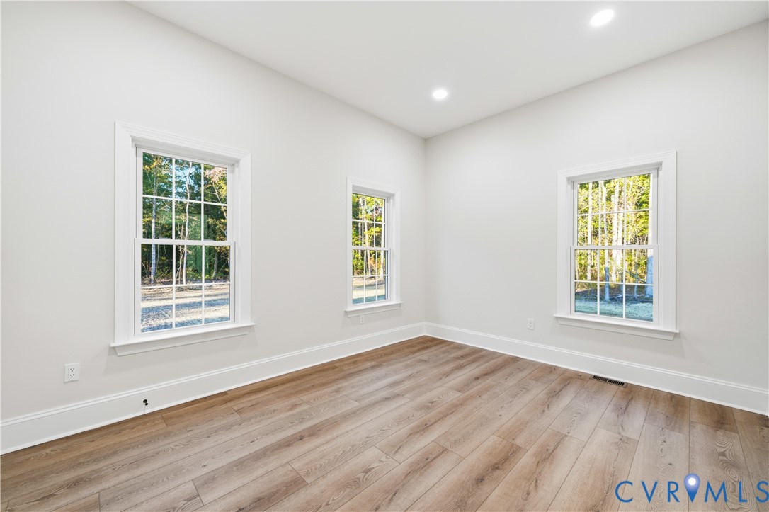 Room interior featuring wood-finish flooring, white walls, recessed ceiling lighting, and three double-hung windows