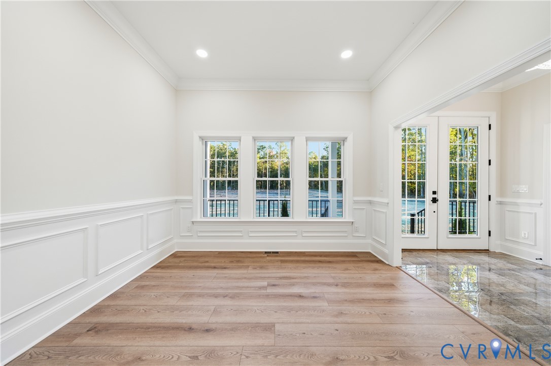 Room featuring wood-finish flooring, wainscoting, crown molding, recessed lighting, and a set of glass-paned double doors