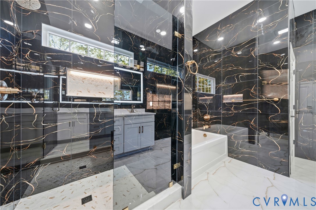 Bathroom featuring black large-format wall tile with copper veining, glass-enclosed shower, soaking tub, light gray cabinetry with quartz countertop, and white floor tile