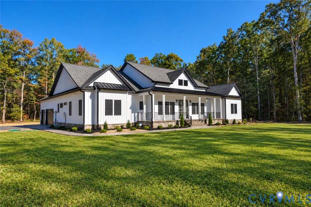 Modern farmhouse exterior featuring vertical white siding, stone veneer foundation accents, black metal roofing, and a full-length covered porch with a metal railing