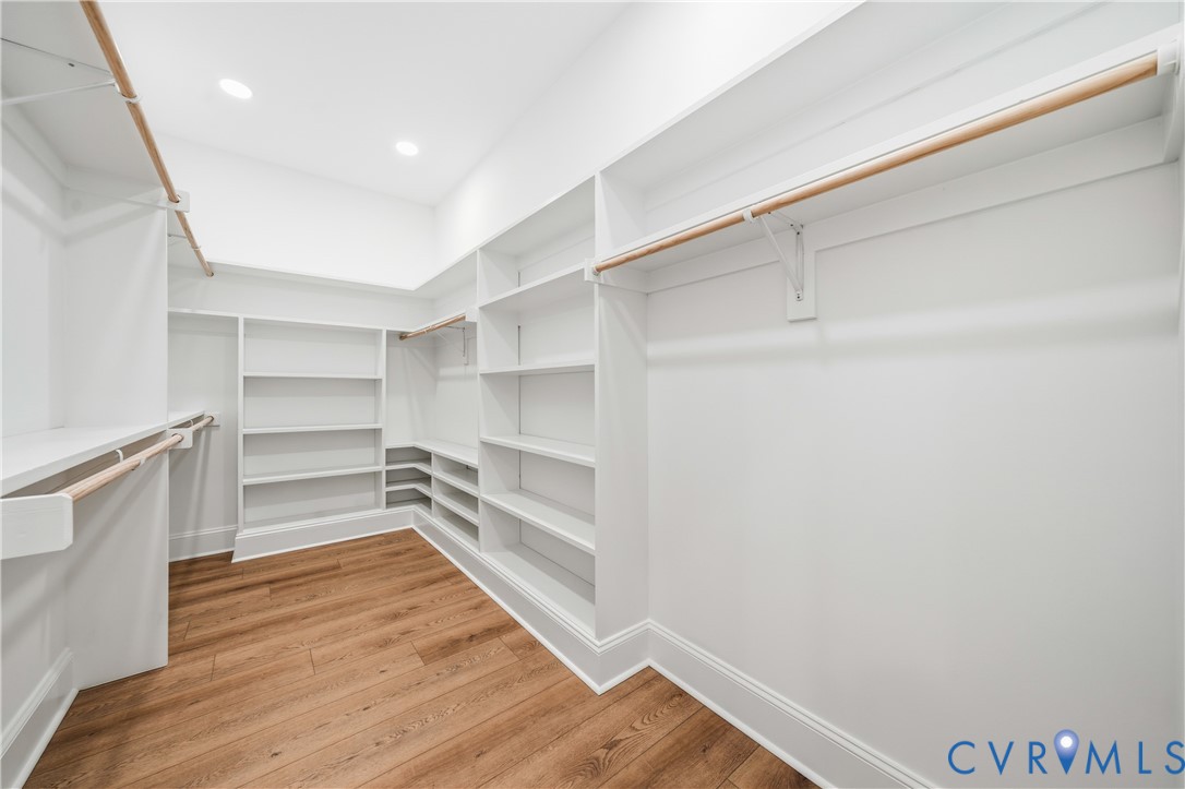 Walk-in closet featuring extensive white built-in shelving, wooden closet rods, recessed ceiling lighting, and wood-finish flooring