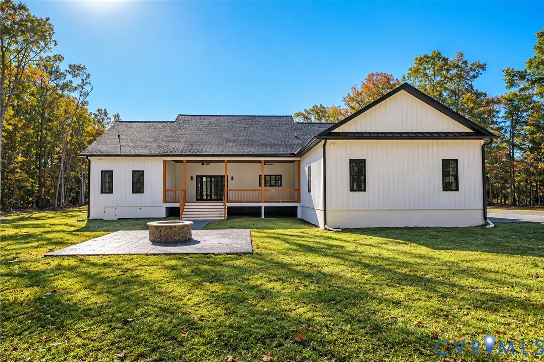 Modern farmhouse exterior featuring vertical board-and-batten siding, a covered porch with timber support columns, and a stamped concrete patio with a circular stone fire pit