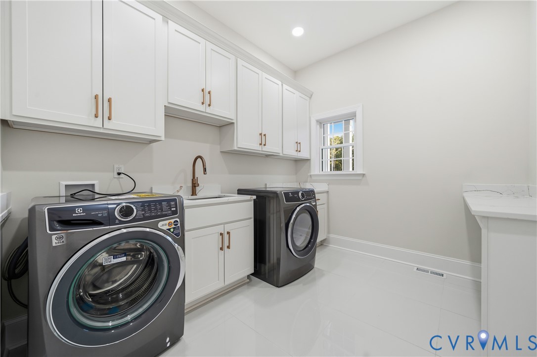 Laundry room featuring white Shaker-style cabinetry, matte bronze hardware, integrated sink, stone-finish countertops, and tile flooring
