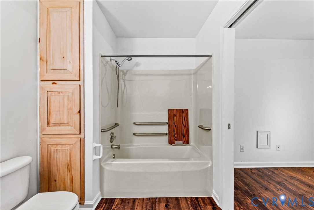 Full-height natural wood cabinetry, shower and tub combination with metallic grab bars, and wood-finish flooring