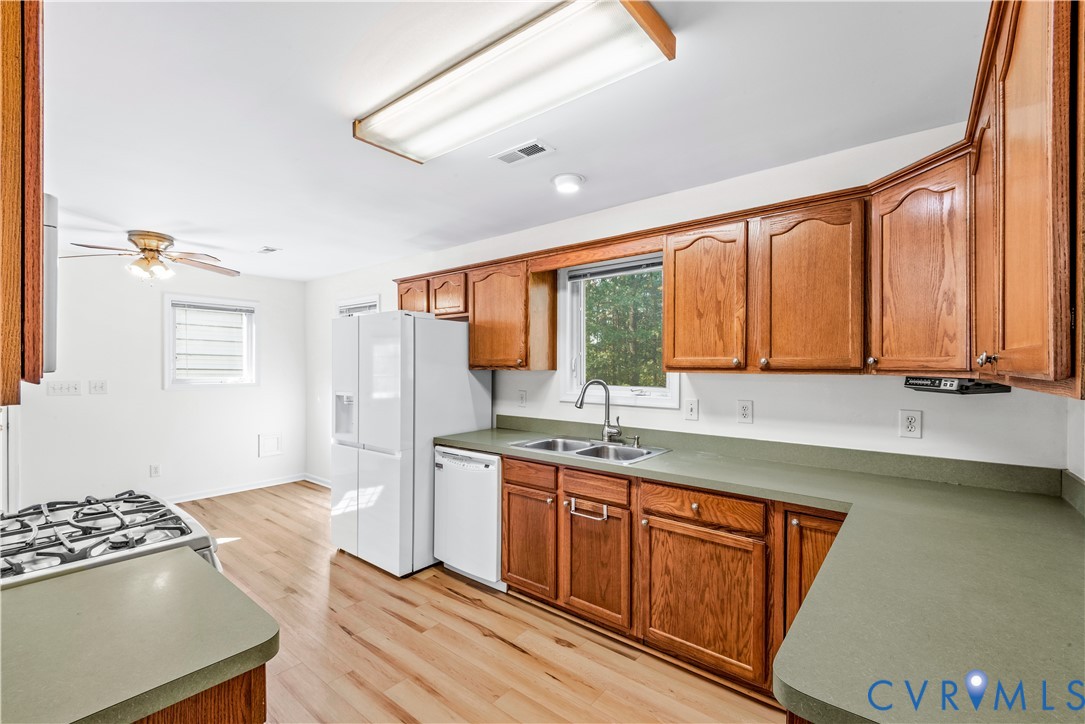 Kitchen featuring wood cabinetry, solid-surface countertops, dual-basin stainless steel sink, gas cooktop, and wood-finish flooring