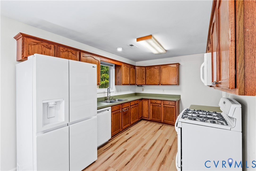 Kitchen featuring wood-finish cabinetry, solid surface countertops, wood-finish flooring, and a stainless steel double-basin sink with a pull-down faucet
