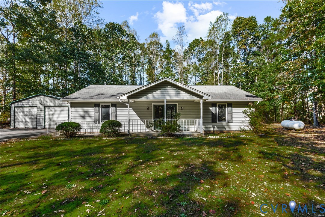 Single-story residence featuring vinyl siding, a covered front porch, a detached two-car garage, and mature tree-lined grounds