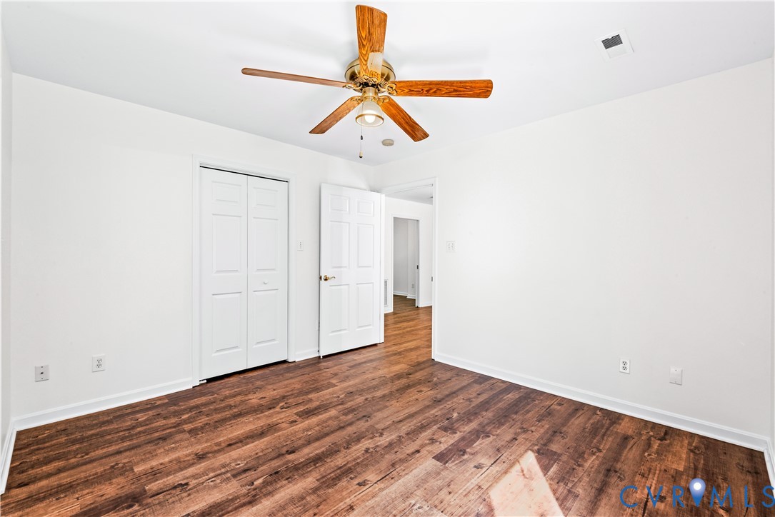 Interior room featuring wood-finish flooring, a centrally mounted ceiling fan with integrated lighting, and white six-panel doors