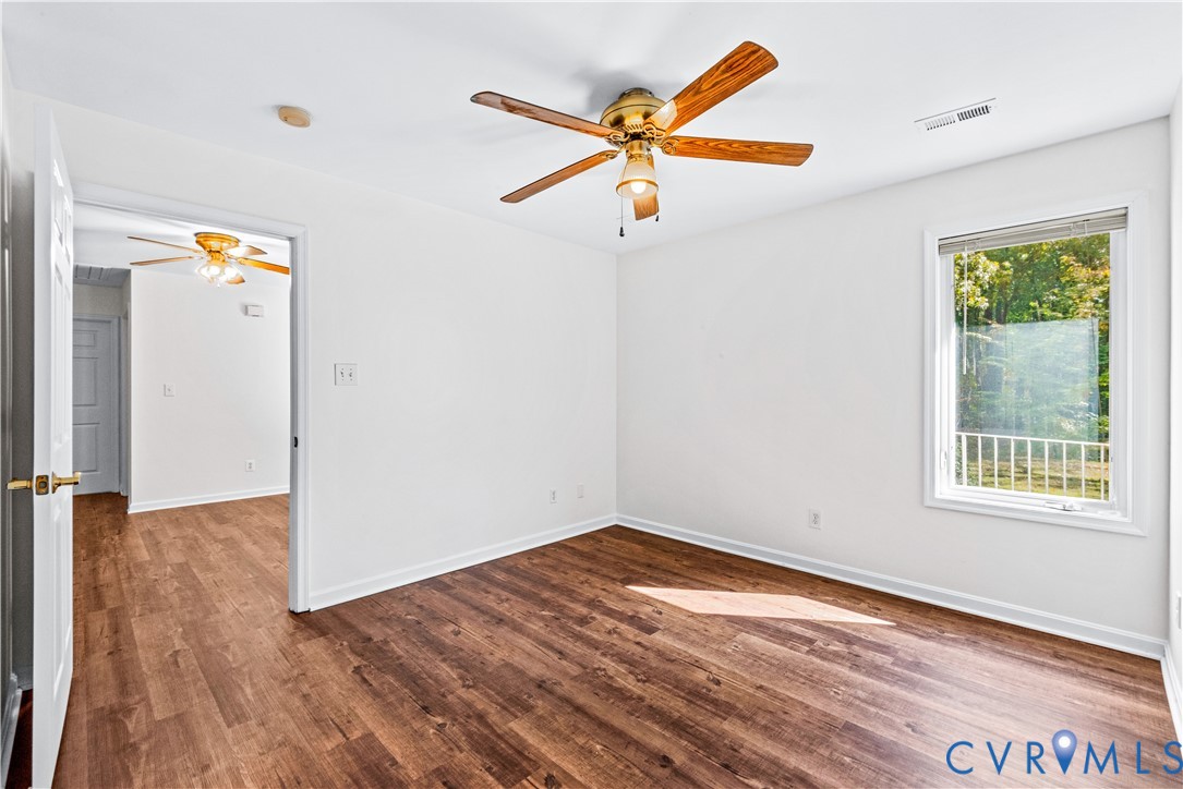 Wood-finish flooring, neutral wall tones, multi-blade ceiling fan, and a double-hung window featuring natural exterior scenery