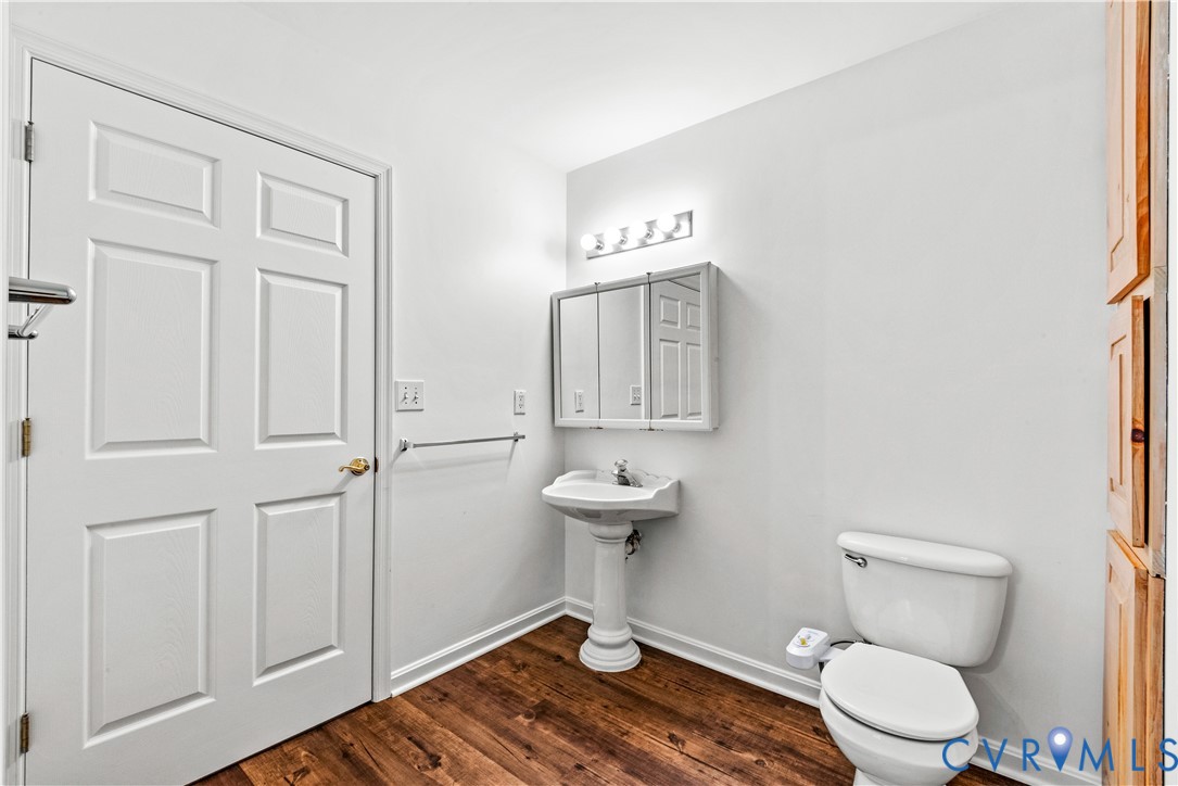 Bathroom featuring wood-finish flooring, a white pedestal sink, a multi-panel mirrored medicine cabinet, a four-light fixture, and built-in wood cabinetry