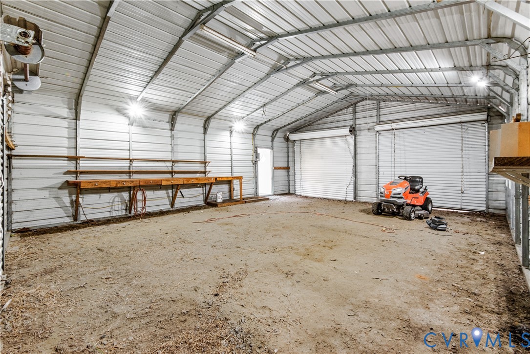 Spacious metal-sided detached garage featuring two roll-up doors, high vaulted ceilings, and a built-in wooden workbench