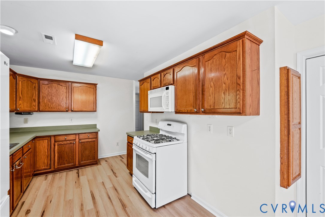 Kitchen featuring wood cabinetry, solid-surface countertops, wood-finish flooring, and white built-in appliances including a gas range and microwave