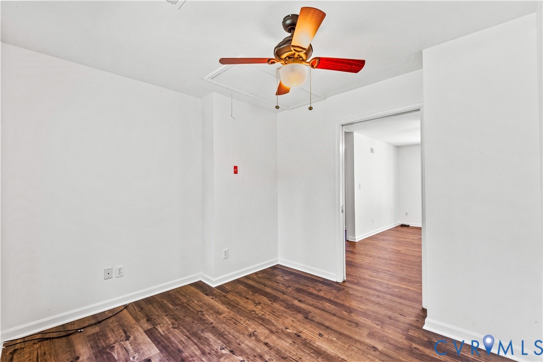 Interior room featuring wood-finish flooring, a ceiling fan with integrated lighting, and a ceiling-mounted attic access panel