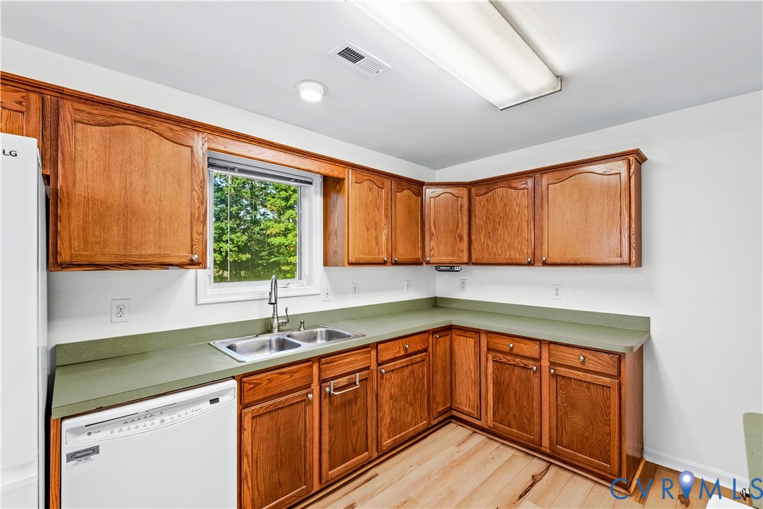 Kitchen featuring wood cabinetry, solid-surface countertops, dual-basin stainless steel sink, wood-finish flooring, and built-in dishwasher