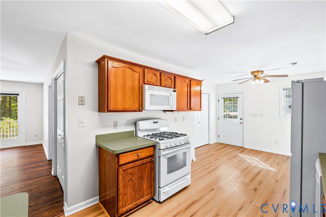 Kitchen featuring wood cabinetry, solid-surface countertops, white gas range with overhead microwave, wood-finish flooring, and a ceiling-mounted light fixture