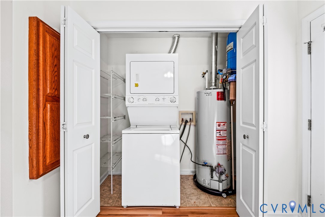 Utility closet containing a stacked laundry unit, vertical water heater, and built-in wire shelving