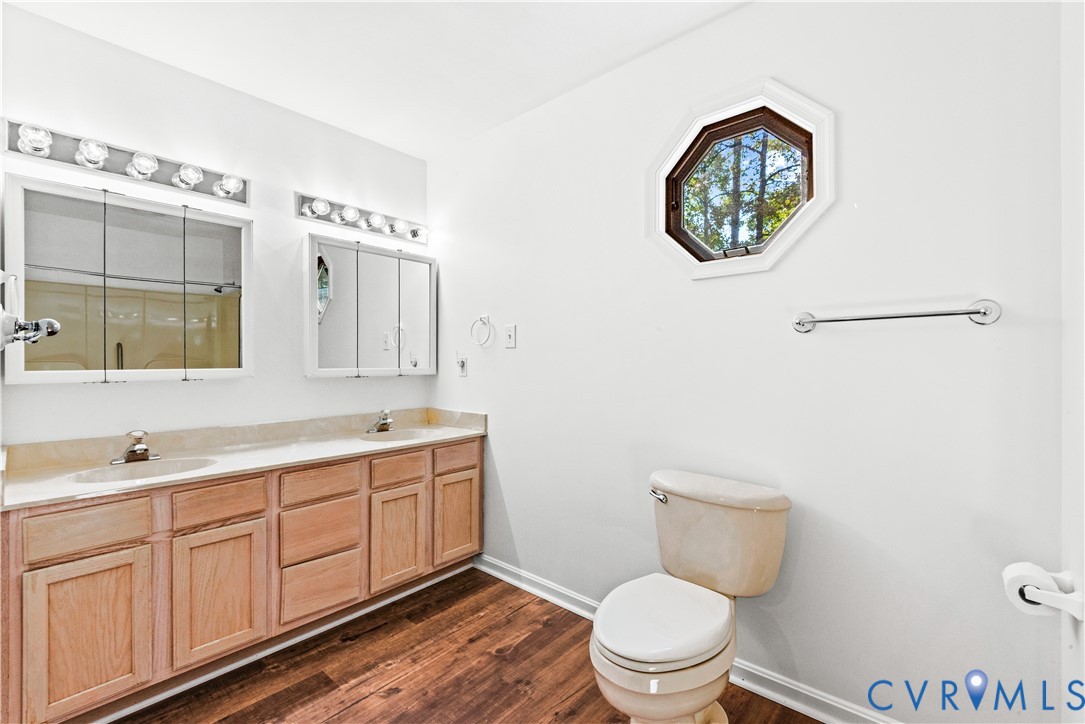 Double vanity featuring wood-finish cabinetry, integrated dual sinks, mirrored medicine cabinets, and decorative wall lighting, complemented by wood-finish flooring and a geometric accent window