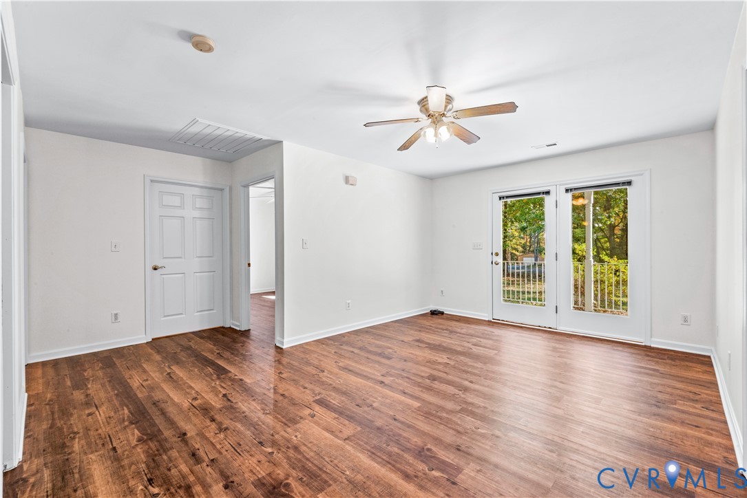 Interior room featuring wood-finish flooring, white walls, a ceiling-mounted light fixture with a fan, and dual-panel glass doors