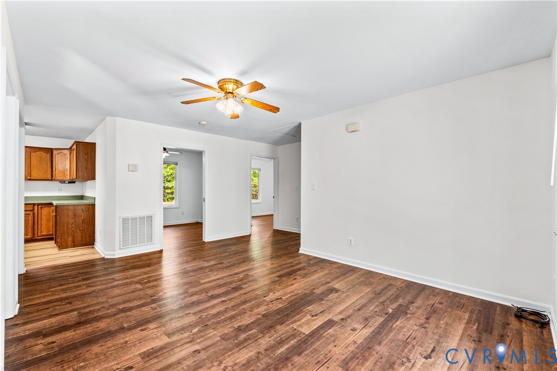 Open interior space featuring wood-finish flooring, a ceiling fan with integrated lighting, and cabinetry with solid-surface countertops