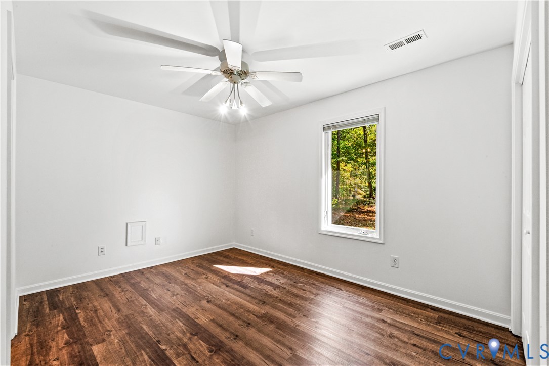 Interior space featuring wood-finish flooring, a multi-blade ceiling fan with integrated lighting, and a single-pane window with a forest exterior