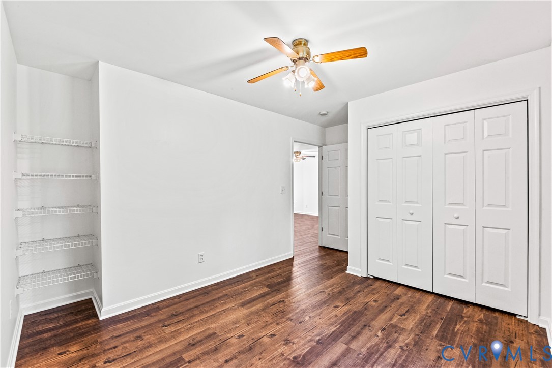 Room featuring wood-finish flooring, built-in wire shelving, a ceiling fan with integrated lighting, and a four-panel bi-fold closet door