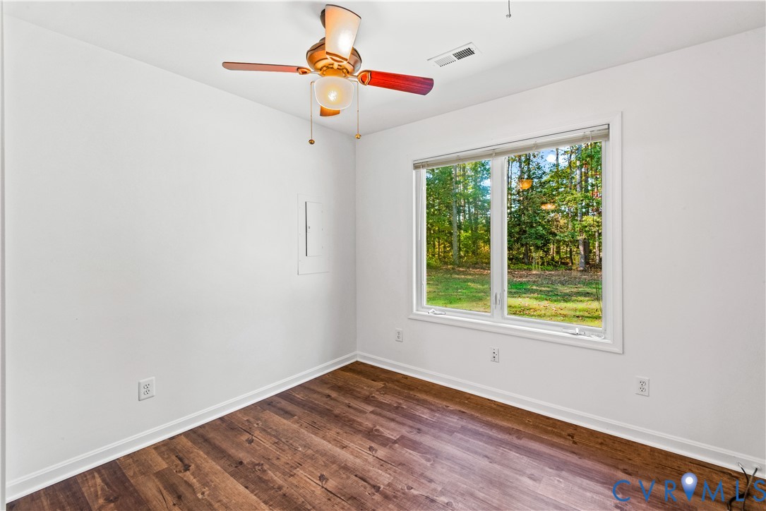 Wood-finish flooring, multi-light ceiling fan, and a large window with woodland backdrop
