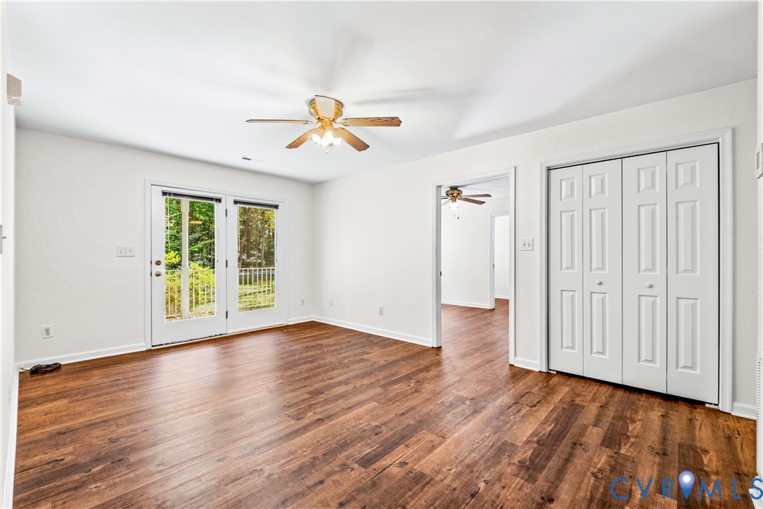 Room featuring wood-finish flooring, dual-panel closet doors, and glass-paned double doors with integrated overhead lighting and ceiling fan