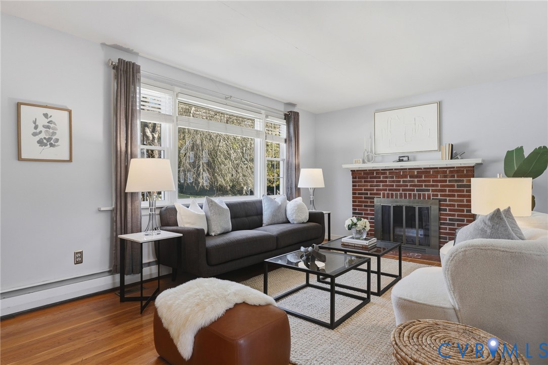 Living area featuring wood-finish flooring, a brick fireplace with a mantel, and a multi-pane window