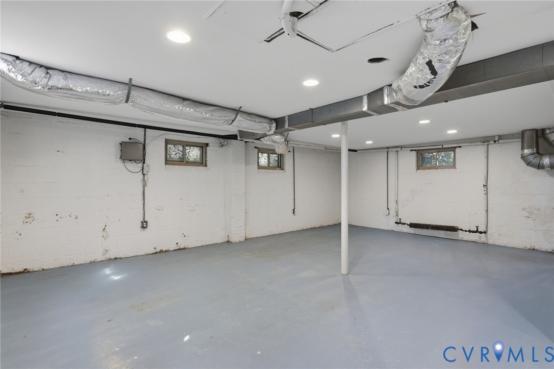 Open-concept interior space featuring painted masonry walls, sealed concrete flooring, recessed lighting, and multiple windows