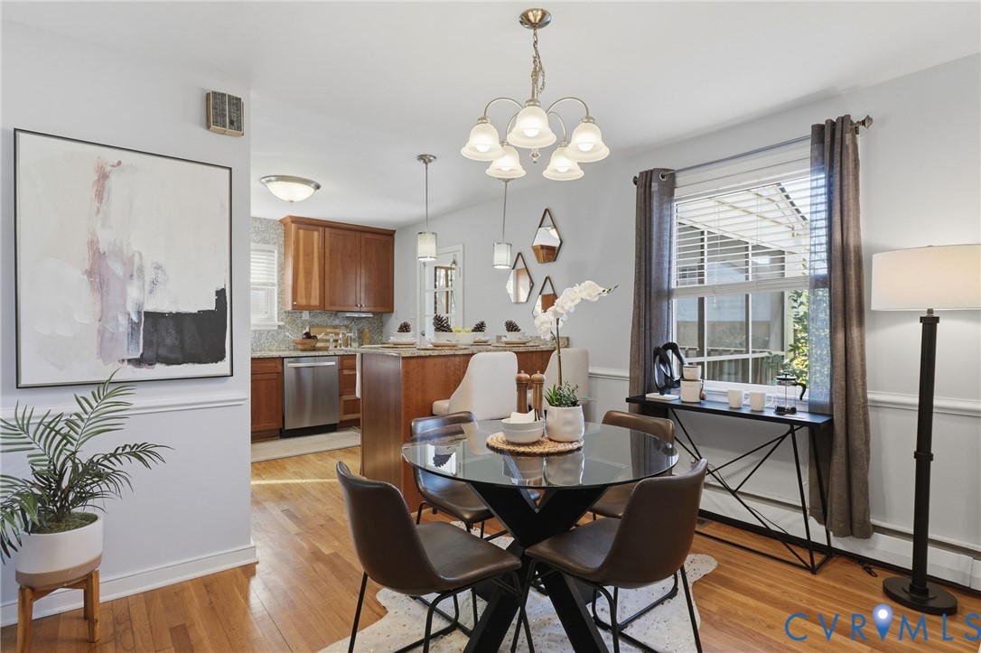 Dining area featuring wood-finish flooring, wainscoting, and a five-light chandelier, with an open kitchen containing wood cabinetry and a breakfast bar