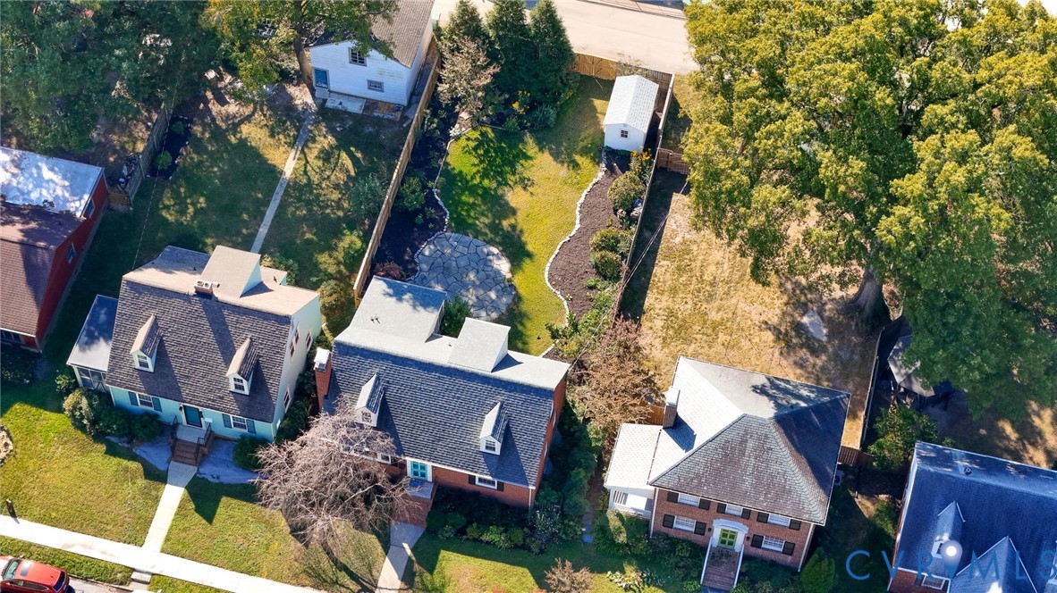 Expansive backyard featuring a fenced perimeter, stone-paver patio, manicured lawn, established shade trees, and a detached storage structure
