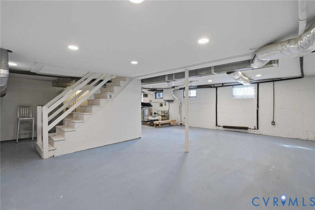 Open-concept area featuring recessed lighting, painted masonry walls, painted stairs with a wooden handrail, and coated concrete flooring