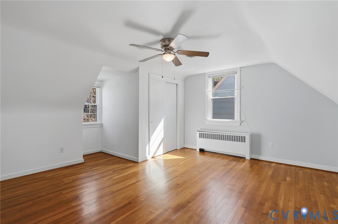 Room featuring wood-finish flooring, vaulted ceilings, dual-pane windows, and a ceiling fan with integrated lighting