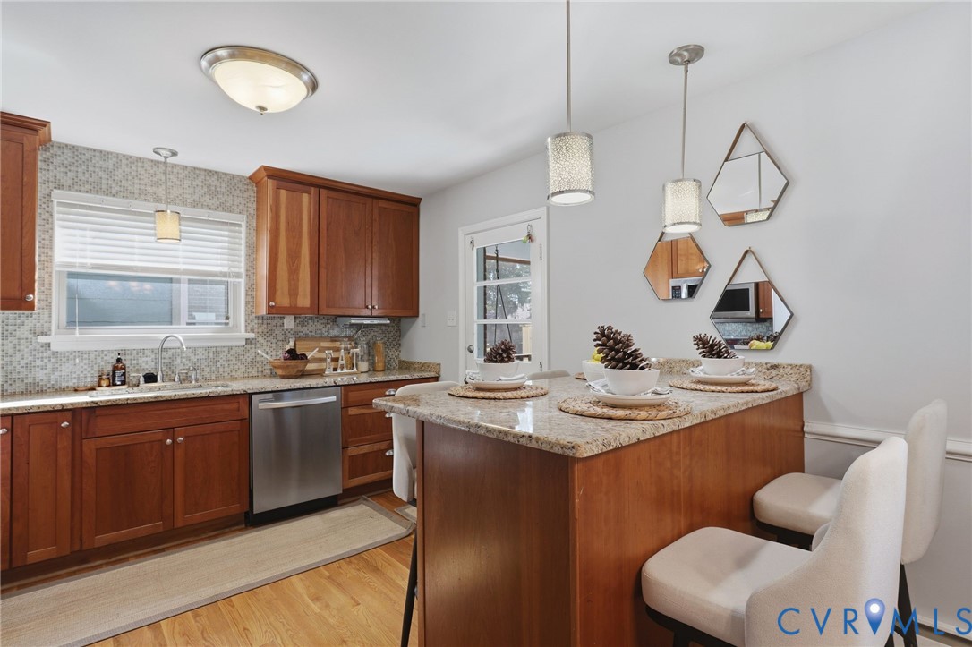 Kitchen featuring wood cabinetry, stone-finish countertops, stainless steel dishwasher, mosaic tile backsplash, and hanging pendant lighting