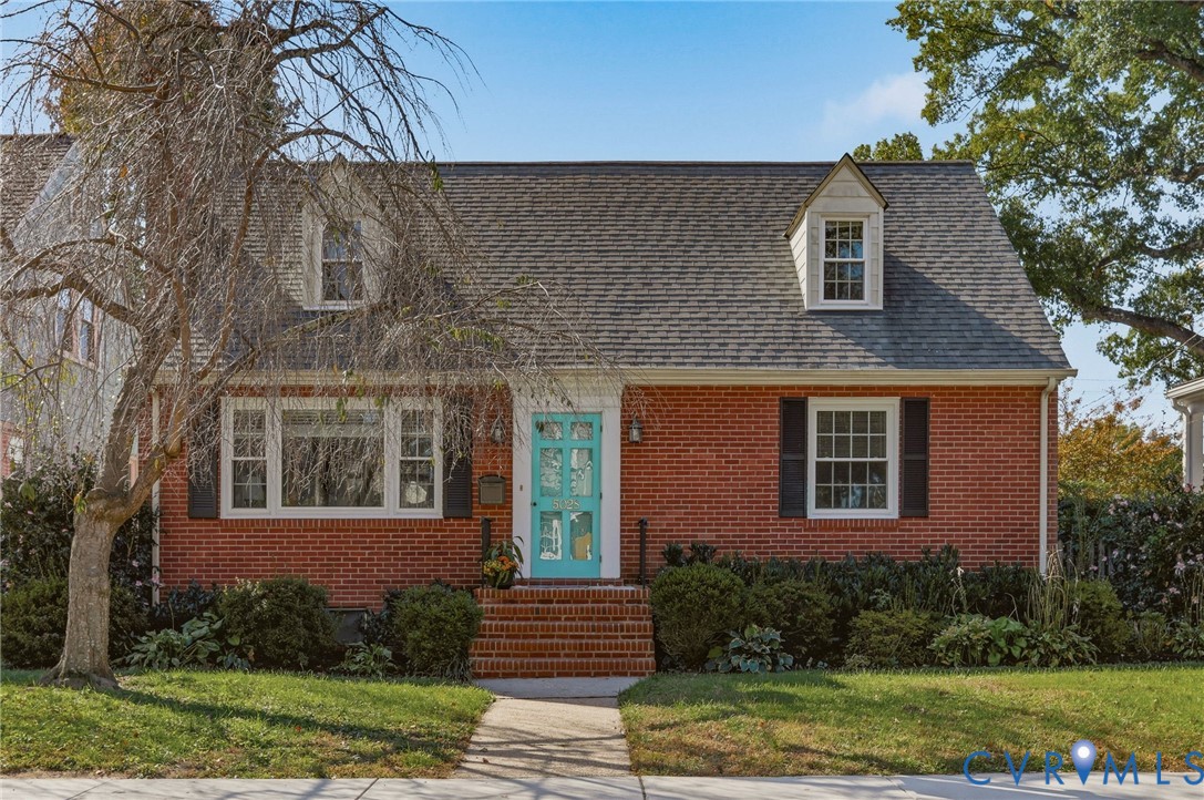 Brick exterior featuring dual dormer windows, shutter-framed windows, and an arched entryway with a paneled door Brick exterior featuring dual dormer windows, shutter-framed windows, and an arched entryway with a paneled door