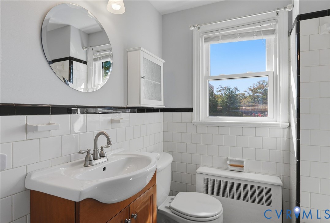 Bathroom featuring a white subway tile surround with black accent tiling, a wood-finish vanity with a drop-in sink, a circular wall-mounted mirror, and a wall-mounted medicine cabinet