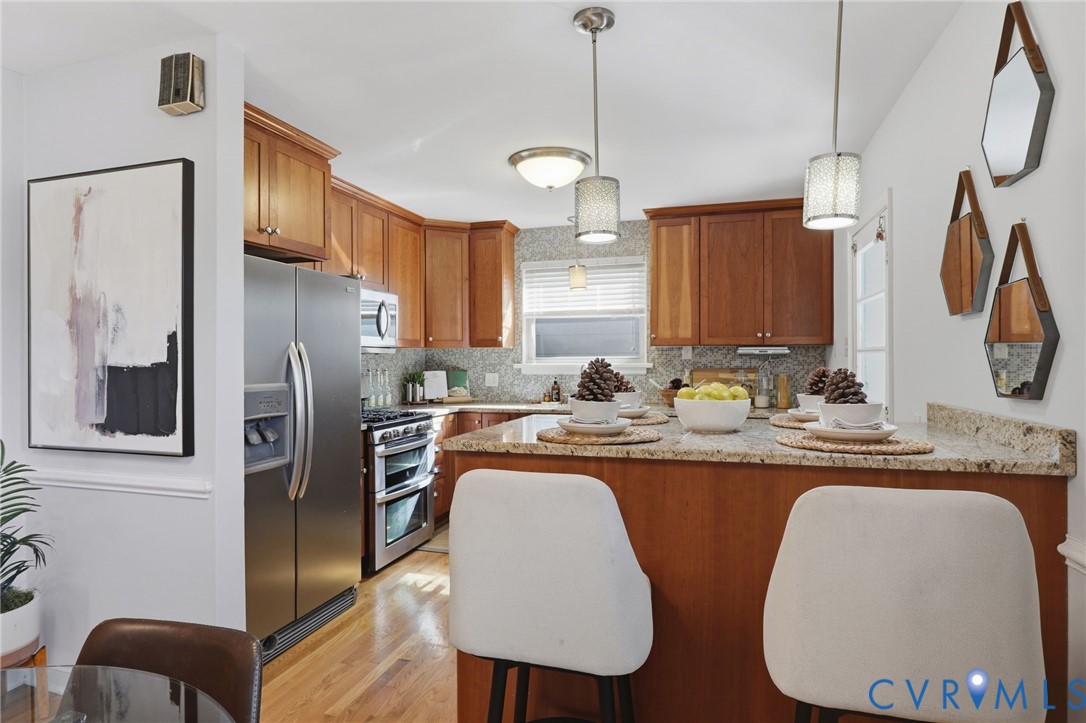 Kitchen featuring natural wood cabinetry, stone countertops, stainless steel appliances, wood-finish flooring, and dual hanging pendant lights