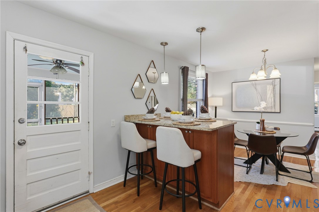 Wood-finish flooring, stone-surfaced kitchen island with built-in cabinetry, dual glass pendant lights, and decorative five-light chandelier