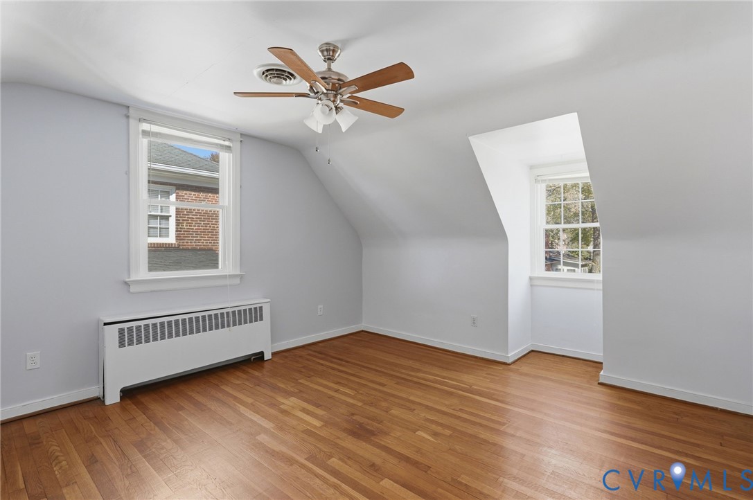 Room featuring wood-finish flooring, dual dormer windows, and a ceiling fan with integrated lighting