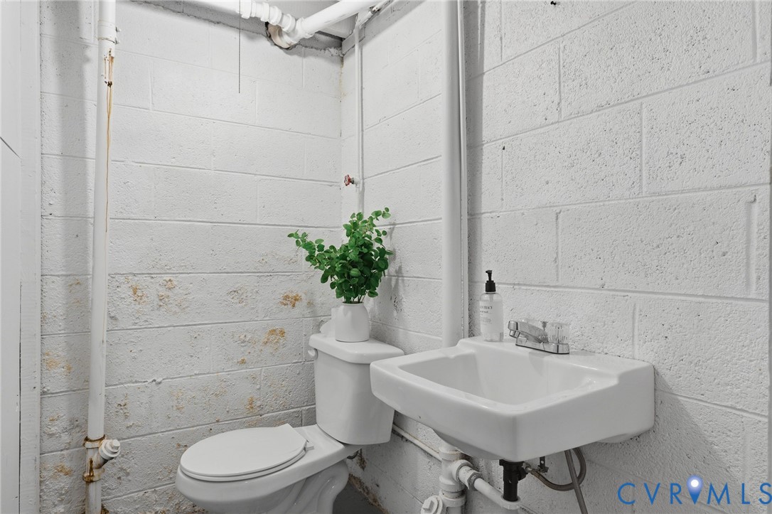 White painted masonry walls featuring a wall-mounted vitreous china sink with a dual-handle chrome faucet and a standard porcelain toilet