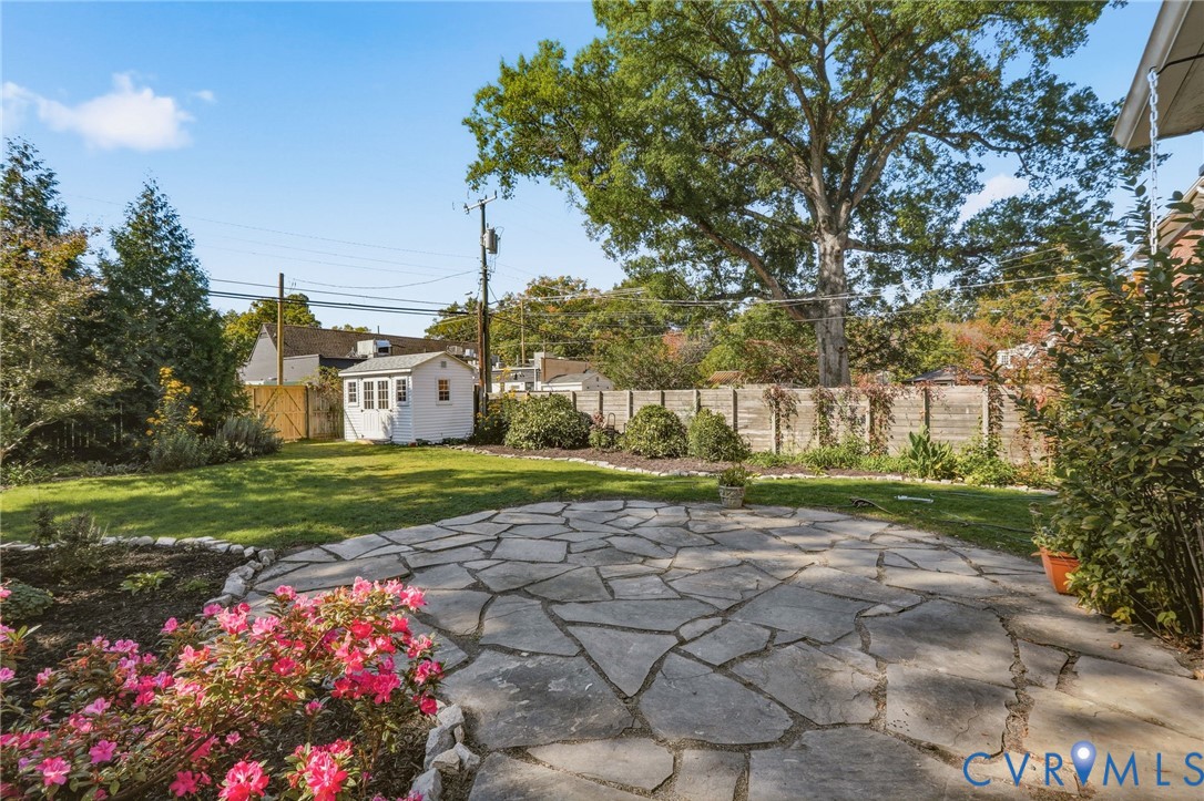 Backyard featuring a flagstone patio, manicured lawn, detached storage structure, mature trees, and perennial garden beds